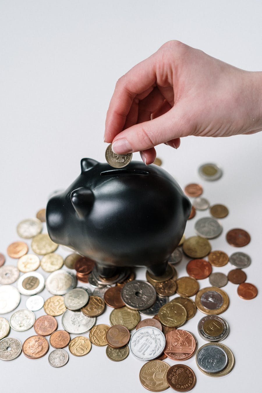 Una mano colocando una moneda en una alcancía rodeada de monedas